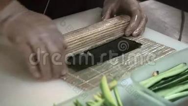 制作和切割橙色寿司卷的过程。 男人用竹垫卷起寿司。 准备好的寿司卷